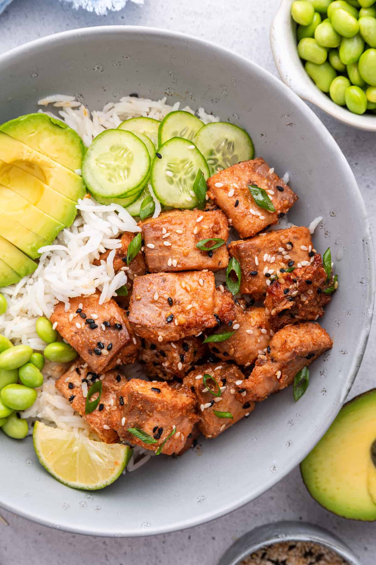 Overhead view of air fryer salmon bites in bowl with rice, cucumbers, edamame, avocado, and lime