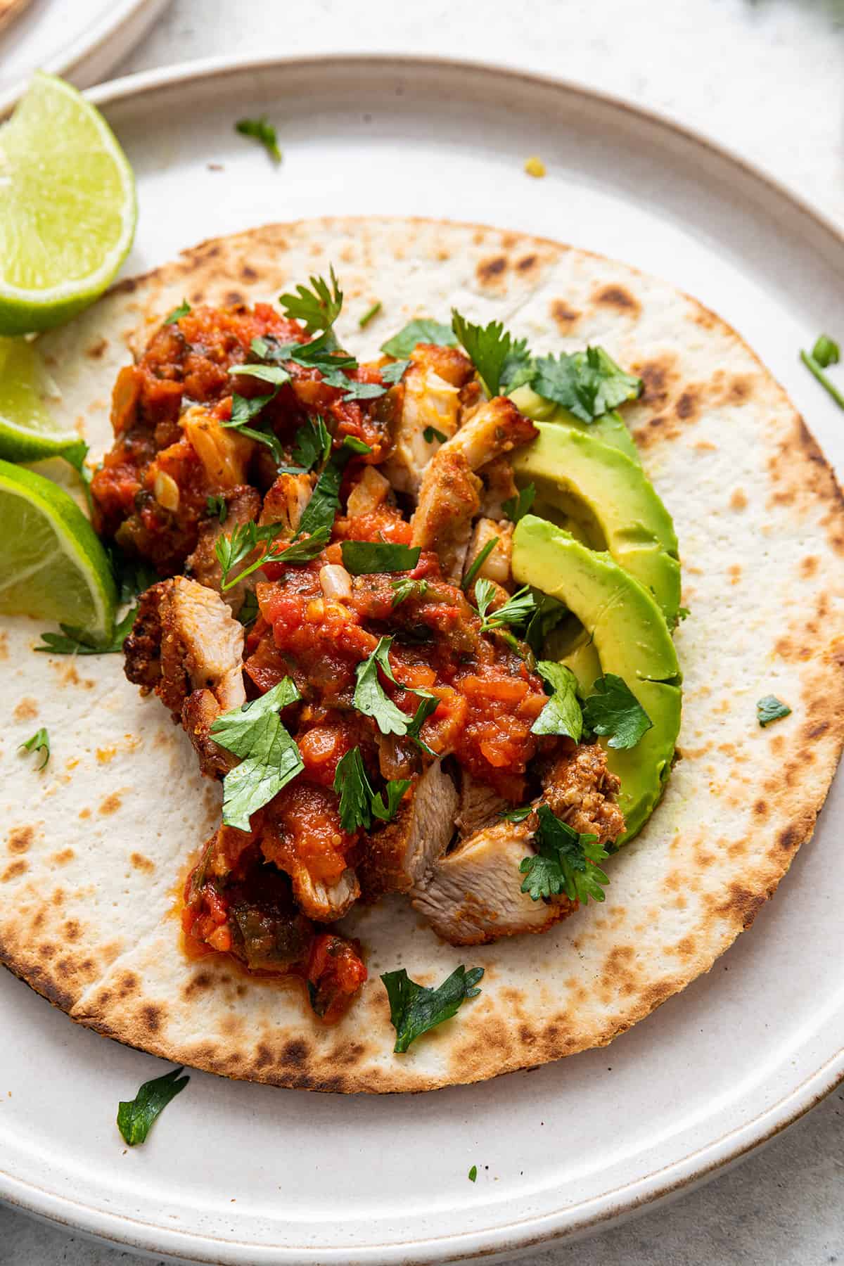 Open blackened chicken taco on plate with sliced avocado, cilantro, and lime wedges
