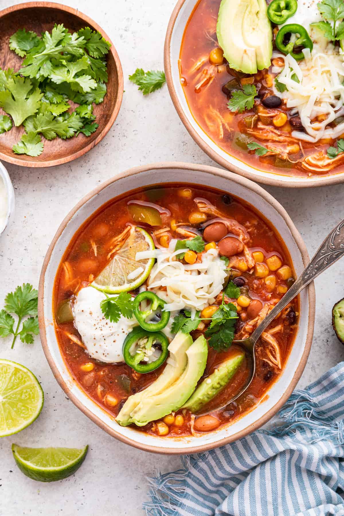 Two bowls of chicken taco soup with small bowl of cilantro leaves
