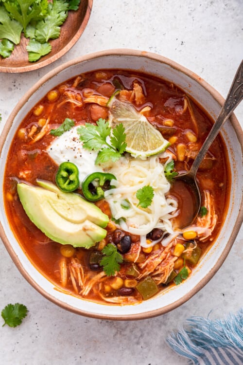 Overhead view of taco soup in bowl, garnished with avocado, cilantro, cheese, sour cream, and lime