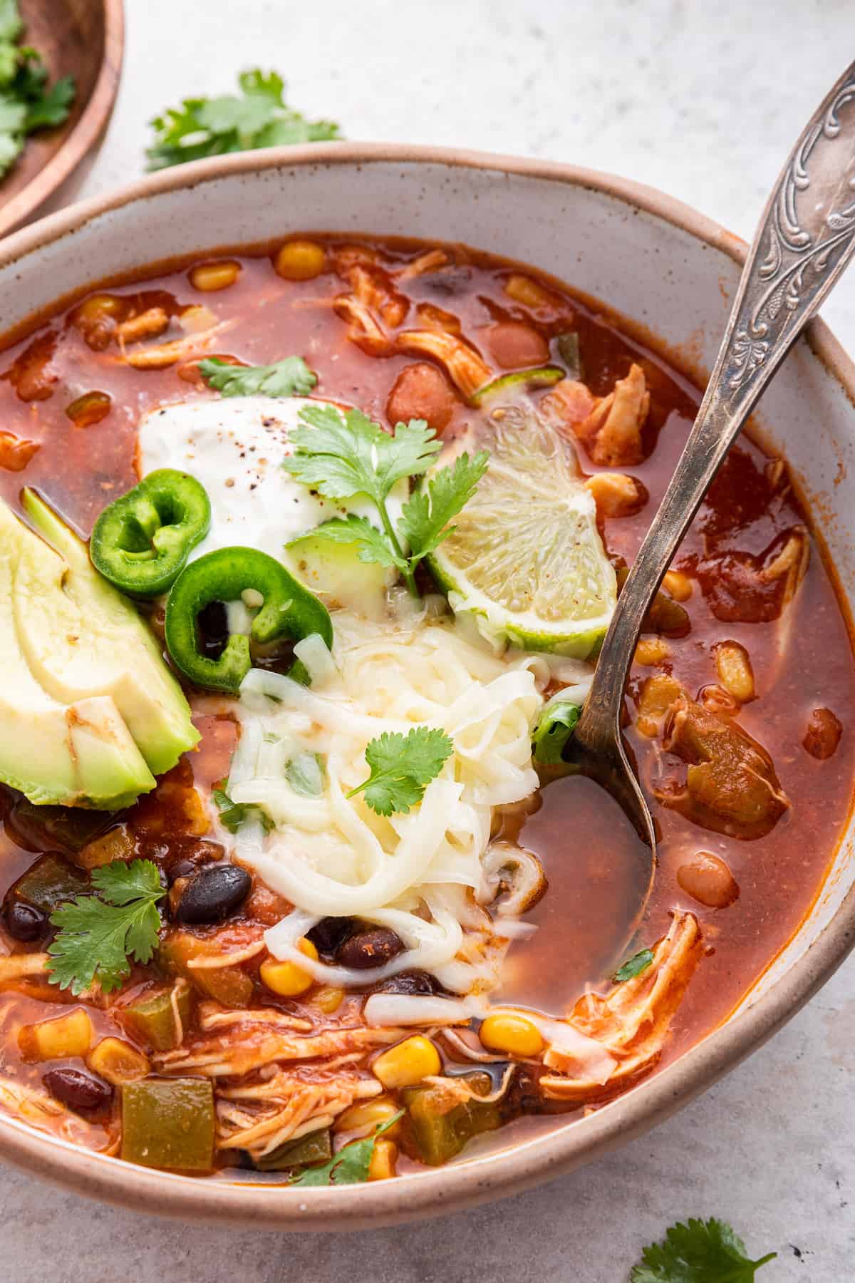 Bowl of chicken taco soup garnished with cheese, avocado, cilantro, and lime