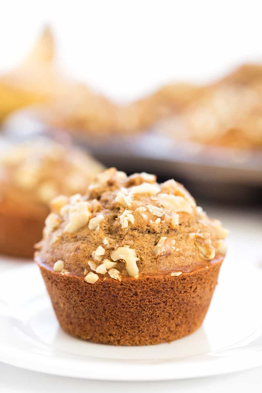 A banana muffin on a white plate, topped with walnuts. 