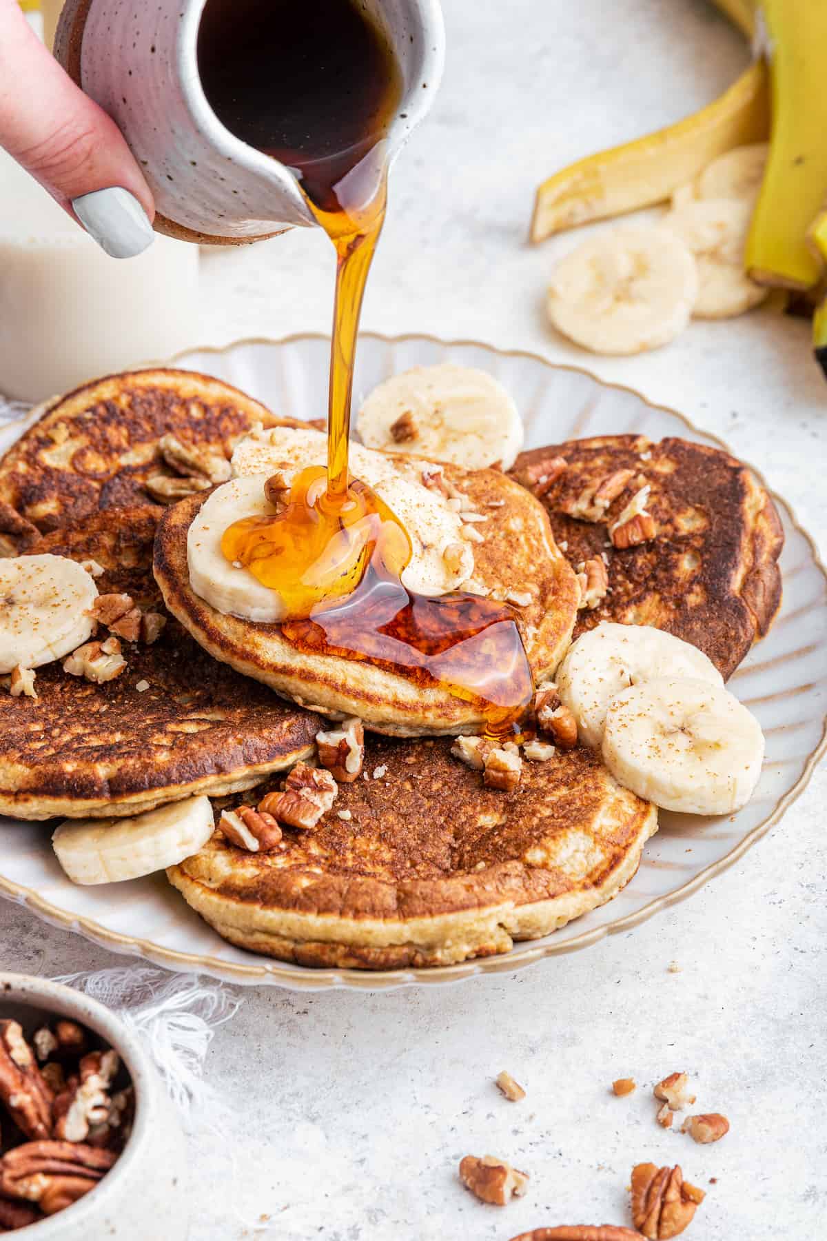 Pouring maple syrup onto plate of oatmeal banana pancakes