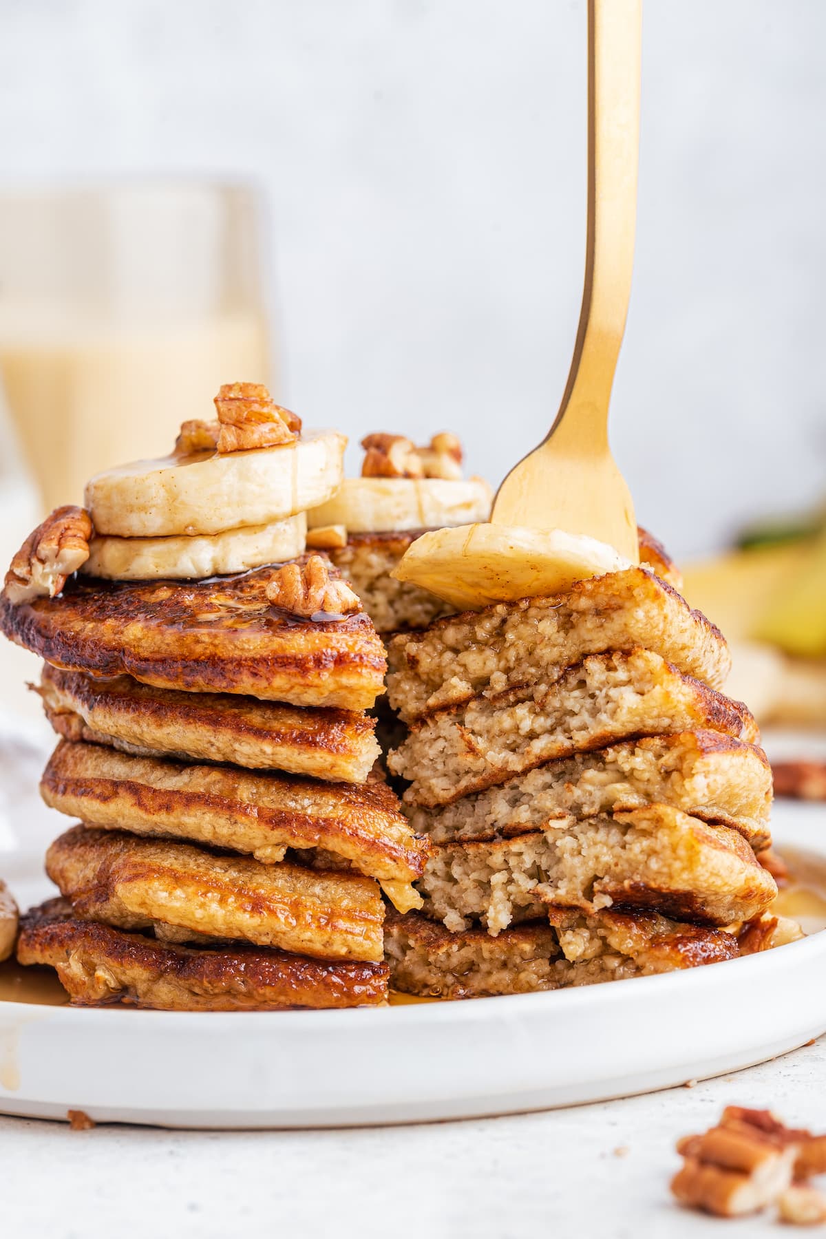 Stack of oatmeal banana pancakes topped with maple syrup, bananas, and pecans