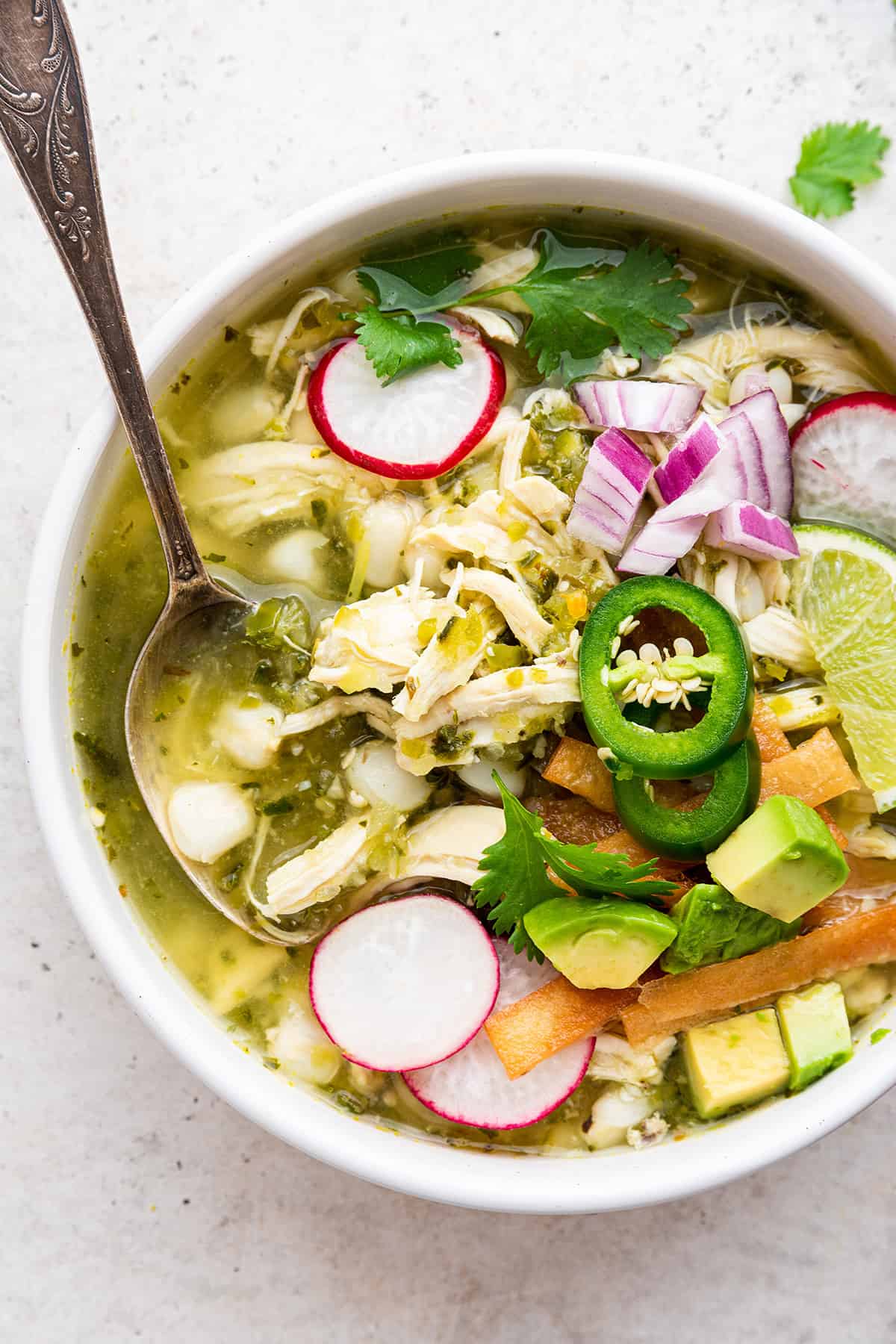 Overhead view of chicken pozole verde in bowl with spoon