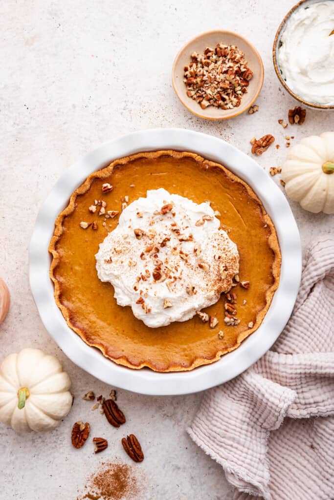 Overhead view of gluten-free pumpkin pie topped with whipped cream, cinnamon, and pecans