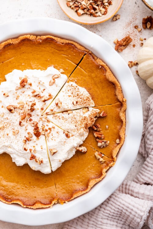 Overhead view of sliced pumpkin pie topped with whipped cream, cinnamon, and nuts