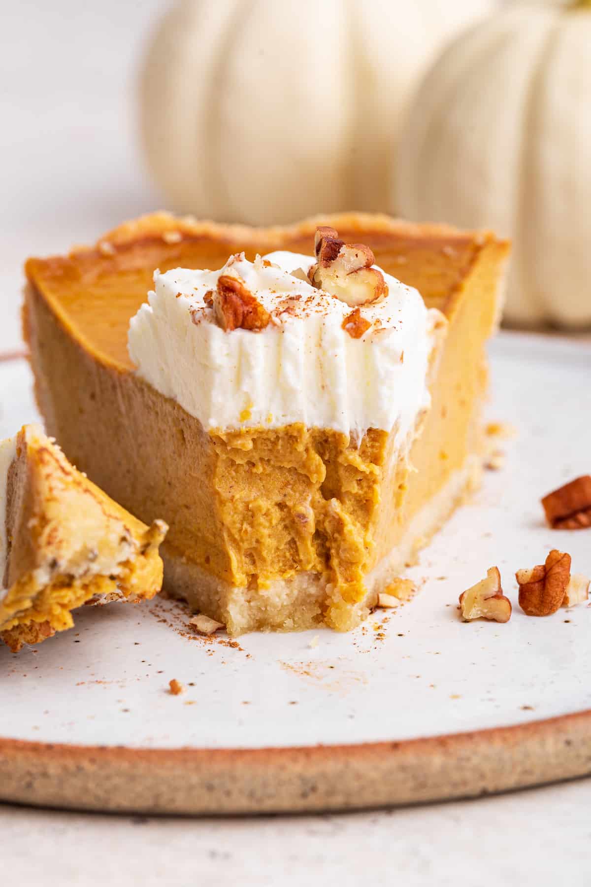 Gluten-free pumpkin pie on plate topped with whipped cream and nuts
