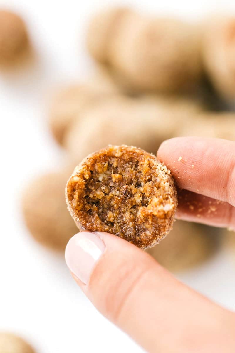 Close up of an apple pie energy ball being held between two fingers and a thumb, with crumbs on the fingers