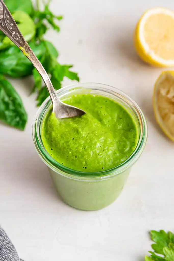 A spoon stuck into a glass filled with green goddess salad dressing.