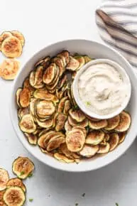 Overhead view of zucchini chips in large bowl with bowl of dip
