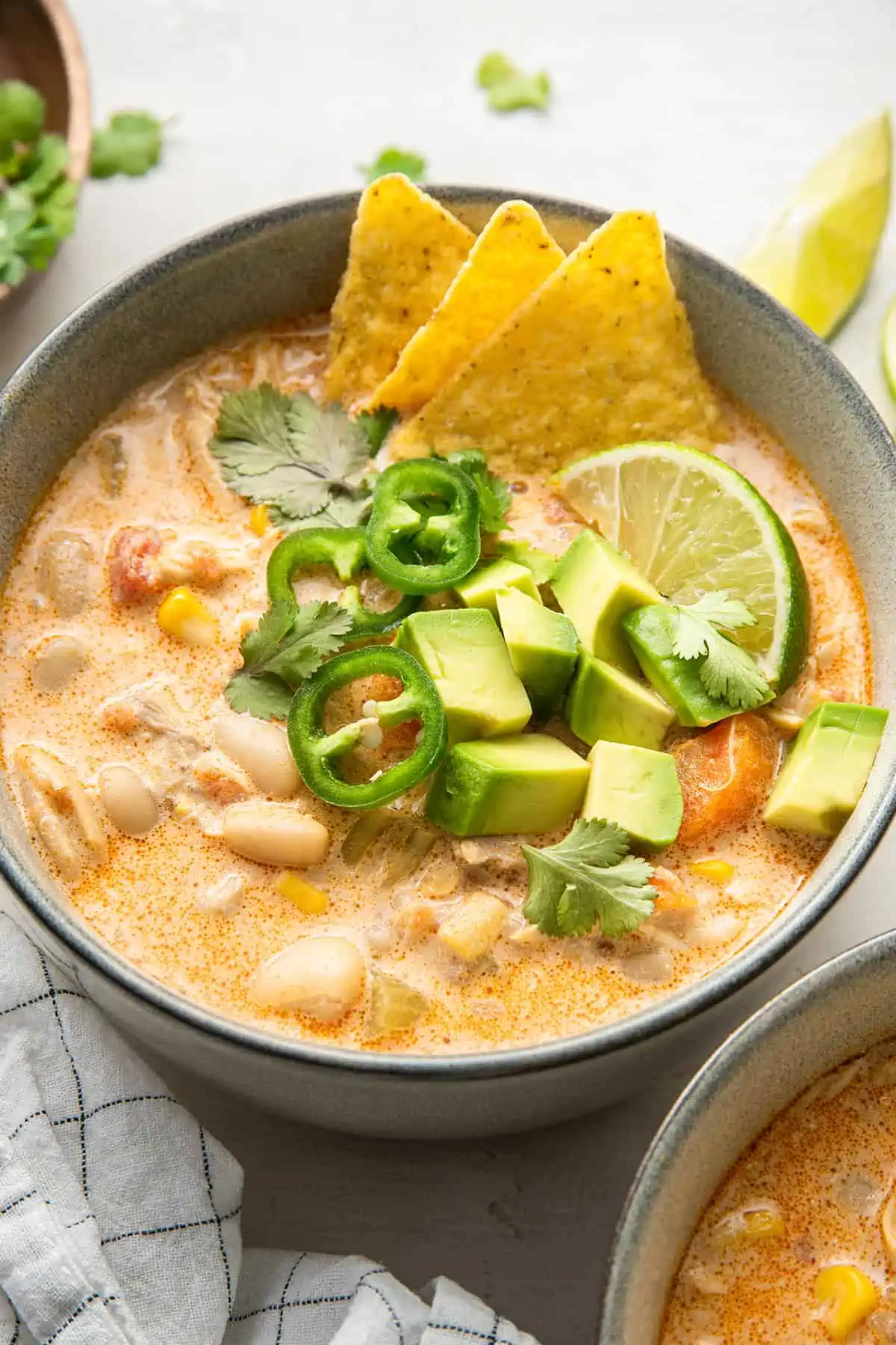 Close up of a bowl of white chicken chili garnished with tortilla chips, a lime wedge, cilantro, and chunks of avocado and chilis